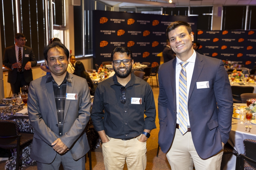 Three men pose together among decorated banquet tables at a UTEP event.